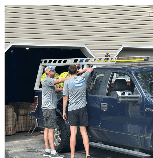 Two men securing ladder to truck.