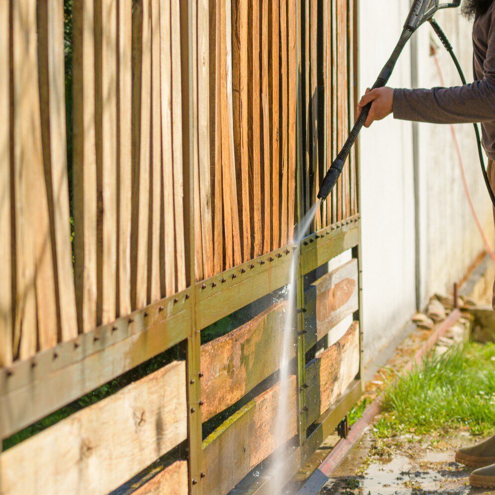 Person pressure washing a wooden fence.