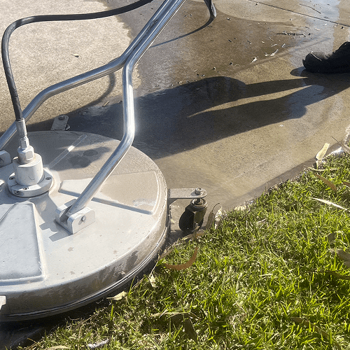 Pressure washing concrete near grass edge.
